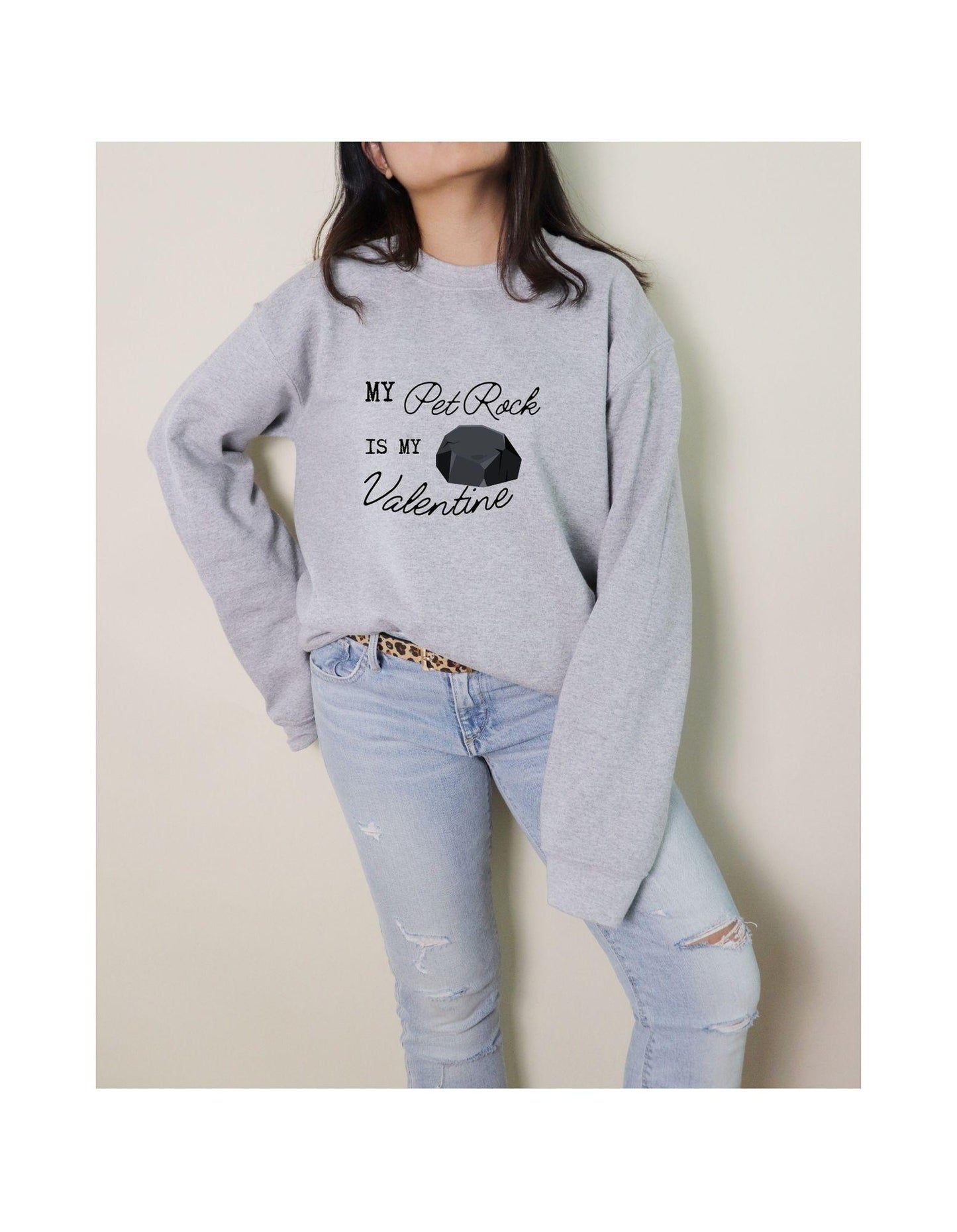 Person wearing a gray sweatshirt with text and light blue jeans against a beige background