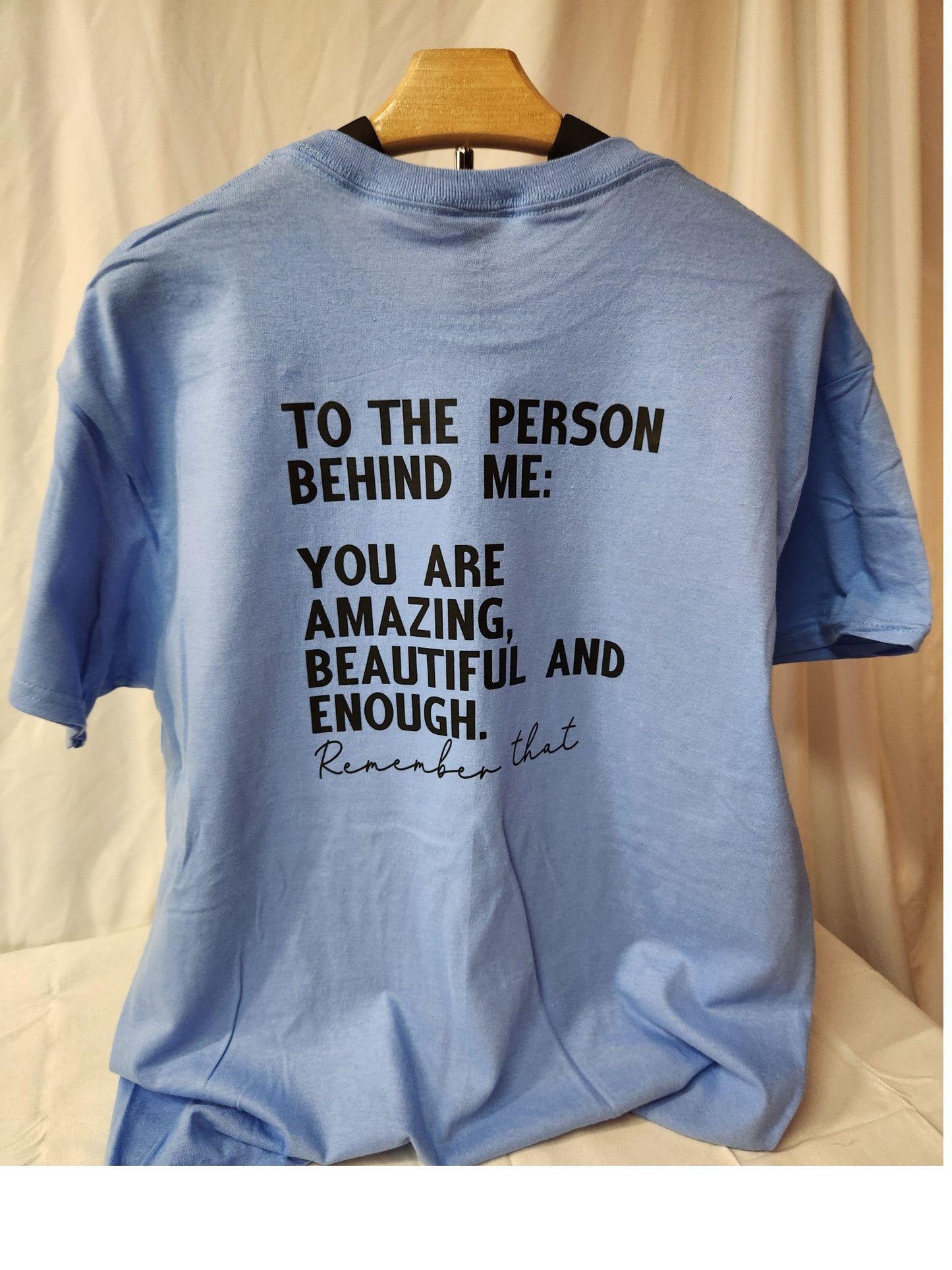Blue t-shirt with motivational message on a wooden hanger against a beige background