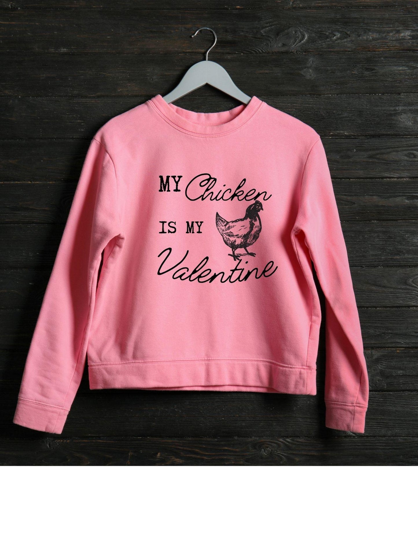 Pink sweatshirt with text and chicken graphic on a wooden background