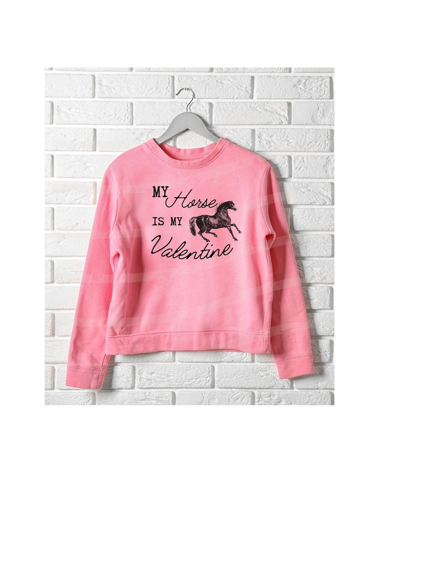 Pink sweatshirt with horse graphic and text on a white brick wall background