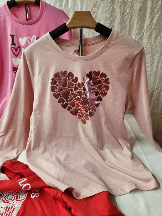 Pink long-sleeve shirt with a heart design on a hanger against a textured wall.