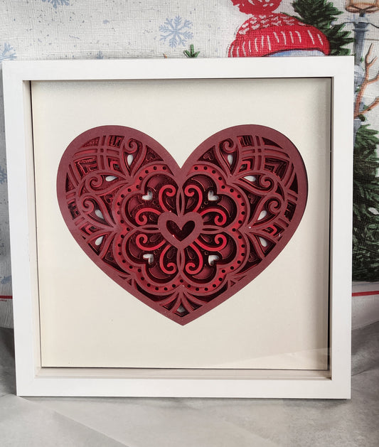 Layered paper heart mandala with tones of red in a white shadow box.