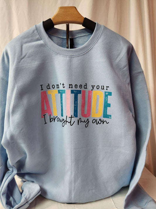 Light blue sweatshirt with colorful text on a wooden hanger against a beige curtain background