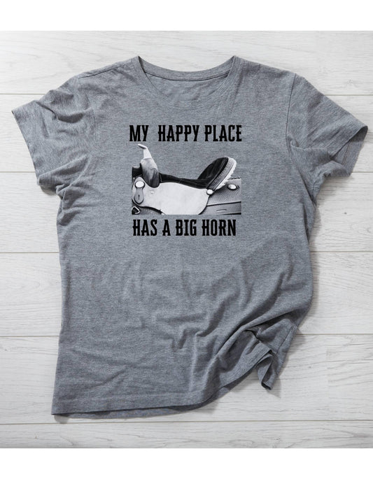 Gray t-shirt with graphic and text 'My happy place has a big horn' on a wooden surface