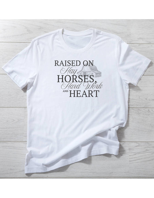 White t-shirt with text 'Raised on Hay, Horses, Hard Work and Heart' on a wooden surface